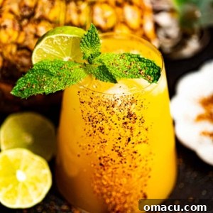 A mango tango drink in a cocktail glass garnished with fresh mint and a lime slice.