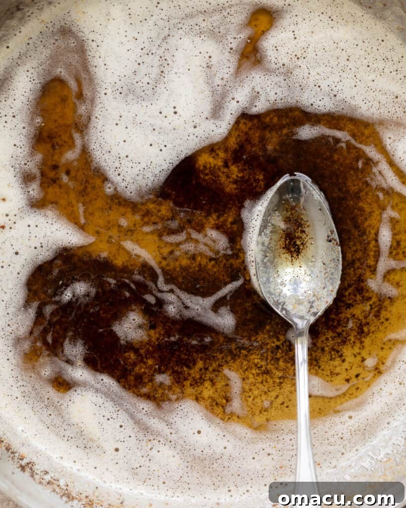 Close-up of golden-brown melted butter in a pan with a spoon, showing the rich color and delicate toasted bits at the bottom.