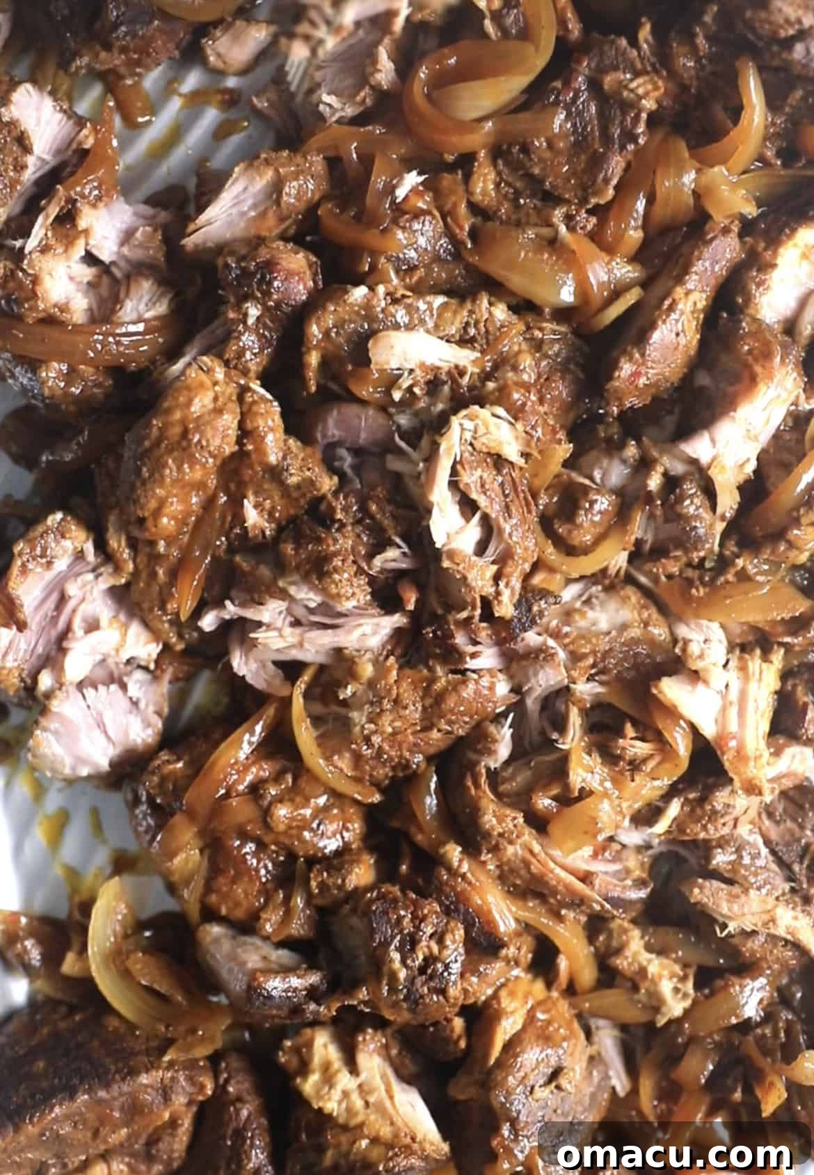 A generous serving of freshly shredded pulled pork on a sheet pan, glistening with rich sauce.