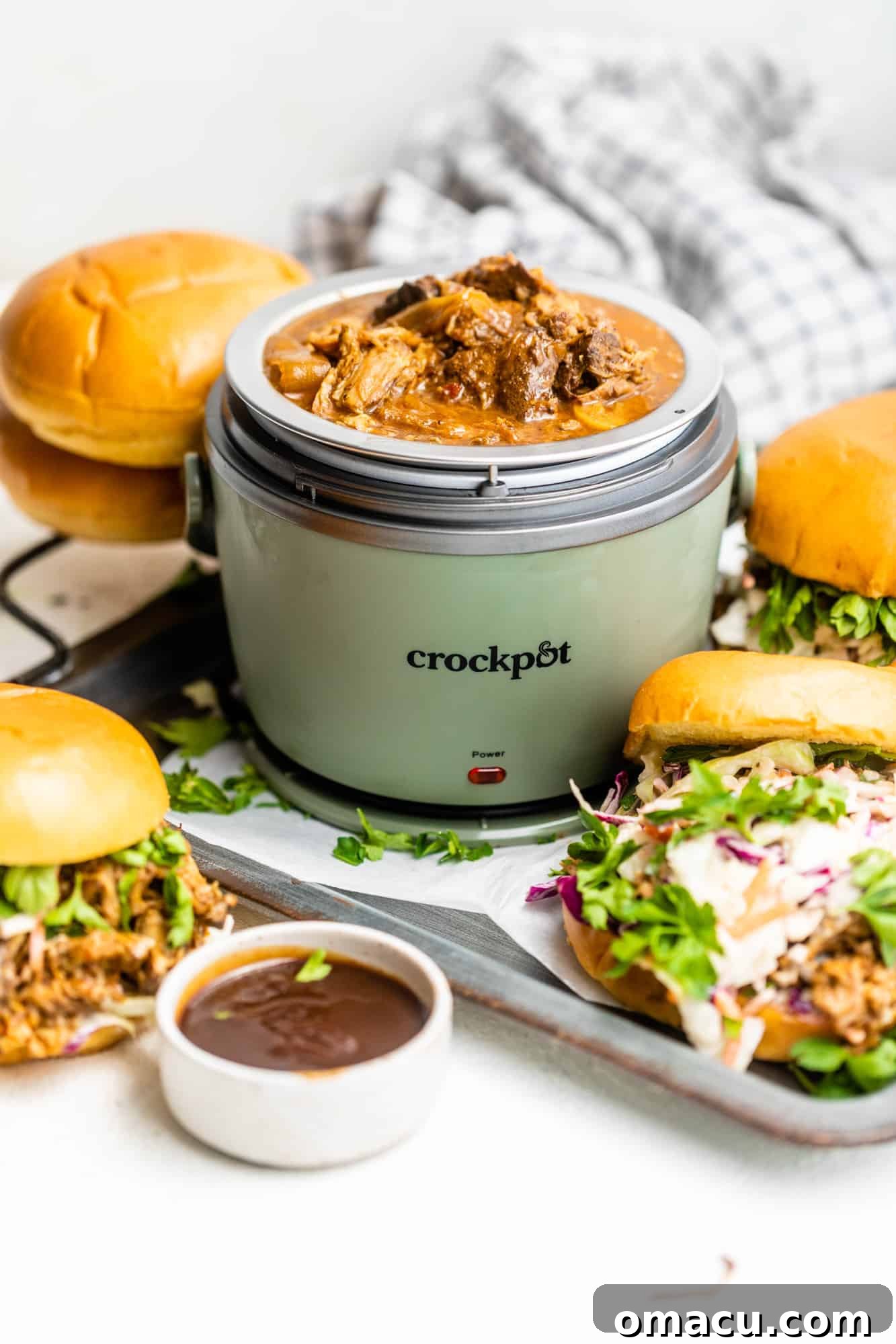 A lunch crock pot filled with BBQ pulled pork, ready to be served with accompanying sandwiches.