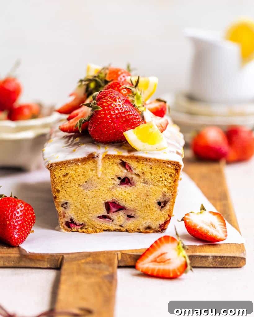 Moist strawberry bread loaf on a wooden board, garnished with fresh strawberry slices, highlighting its tender texture and vibrant fruit chunks.