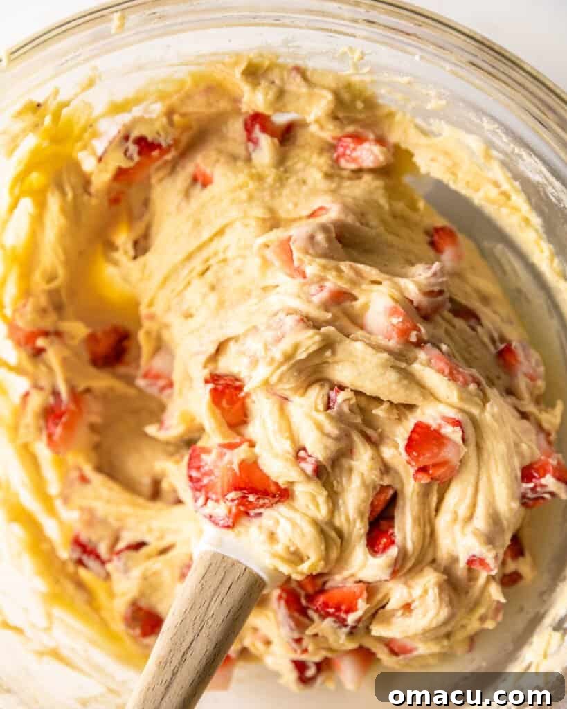 Thick, pink-hued batter for strawberry bread in a large mixing bowl, flecked with strawberry pieces, ready for baking.