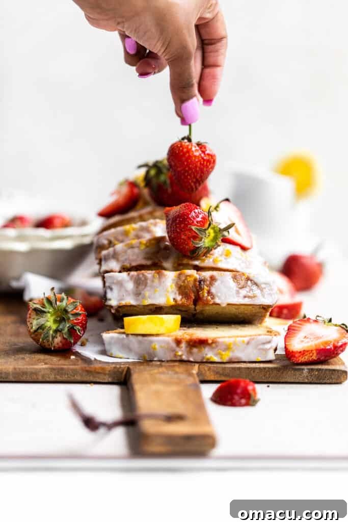 A hand gently placing fresh fruit on top of a baked loaf of strawberry bread, preparing it for serving or glazing.