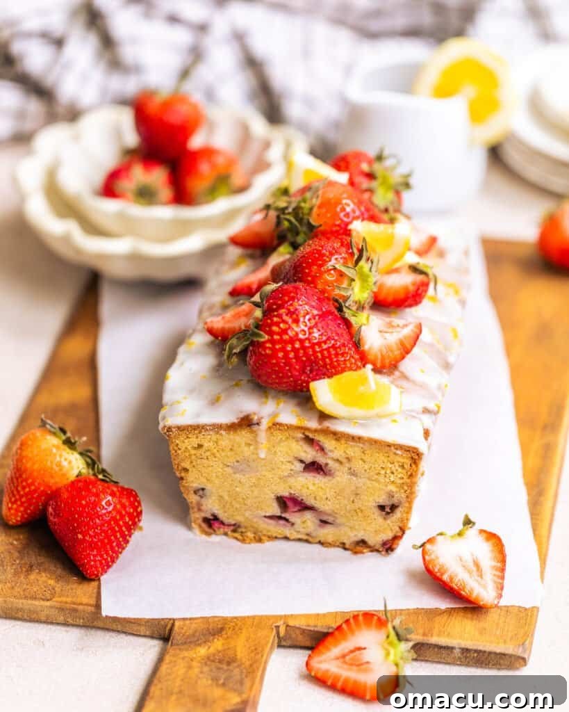 A golden-brown strawberry bread loaf, beautifully sliced to reveal juicy strawberry pieces, positioned in front of a bowl of fresh whole strawberries, emphasizing its natural goodness.