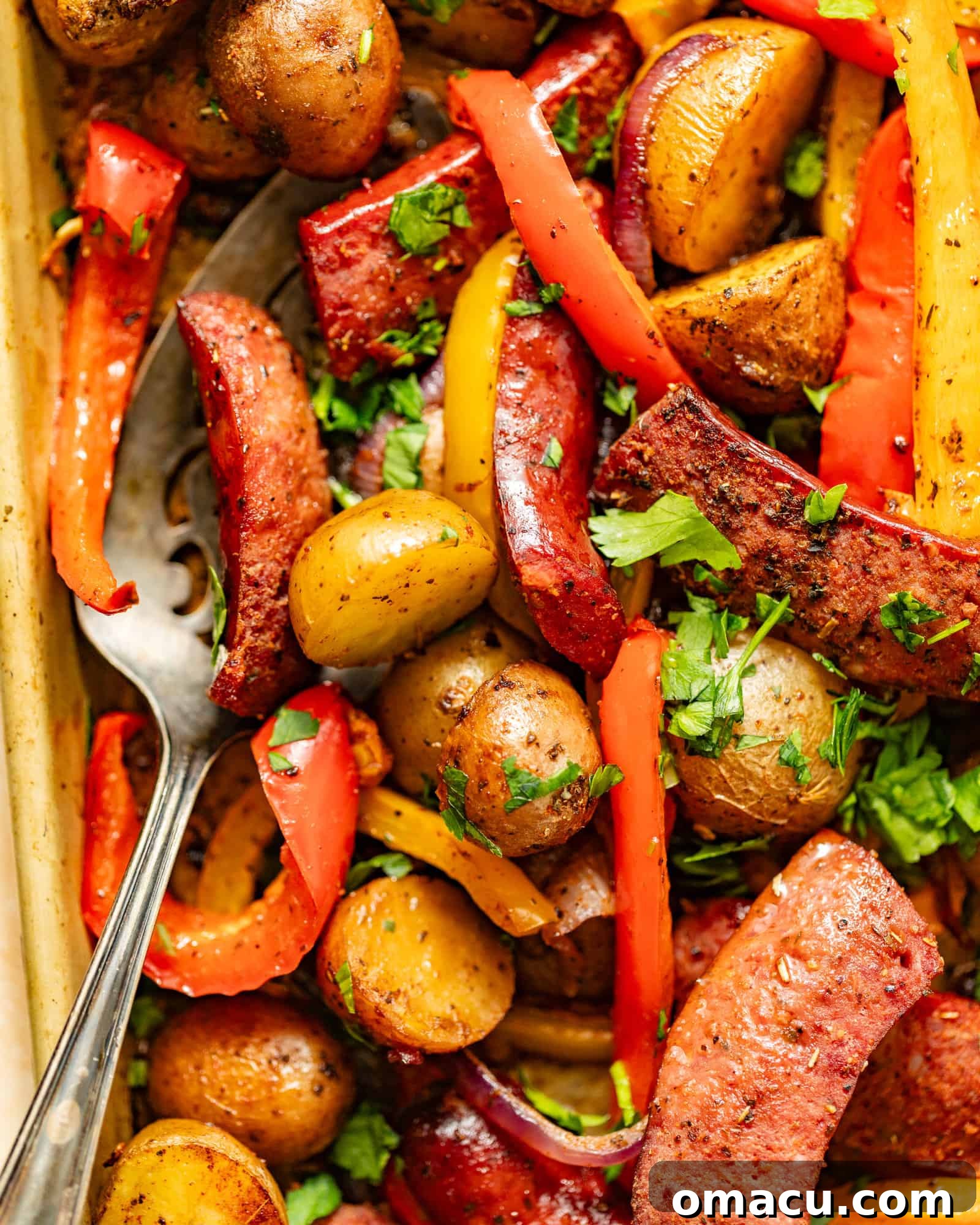 Sausages, peppers, onions, and potatoes arranged on a sheet pan, garnished with fresh parsley.