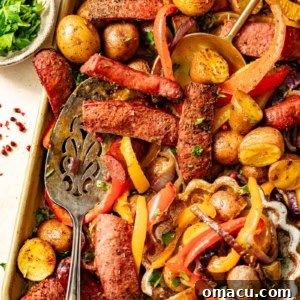 Sausages, peppers, onions, and potatoes on a sheet pan with a bowl of parsley.