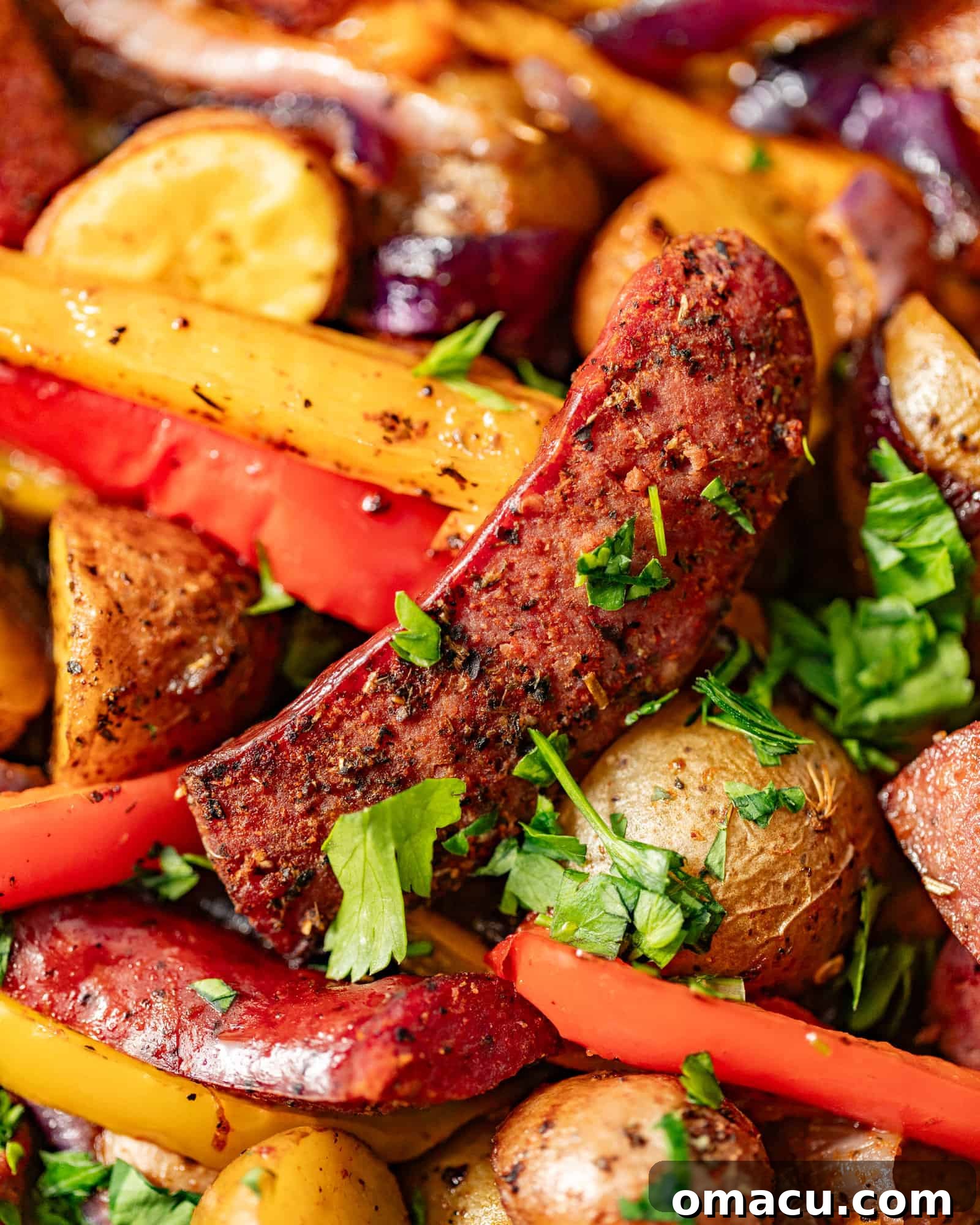 Close-up photo of perfectly roasted sausages and colorful bell peppers on a baking sheet, garnished with fresh chopped parsley.
