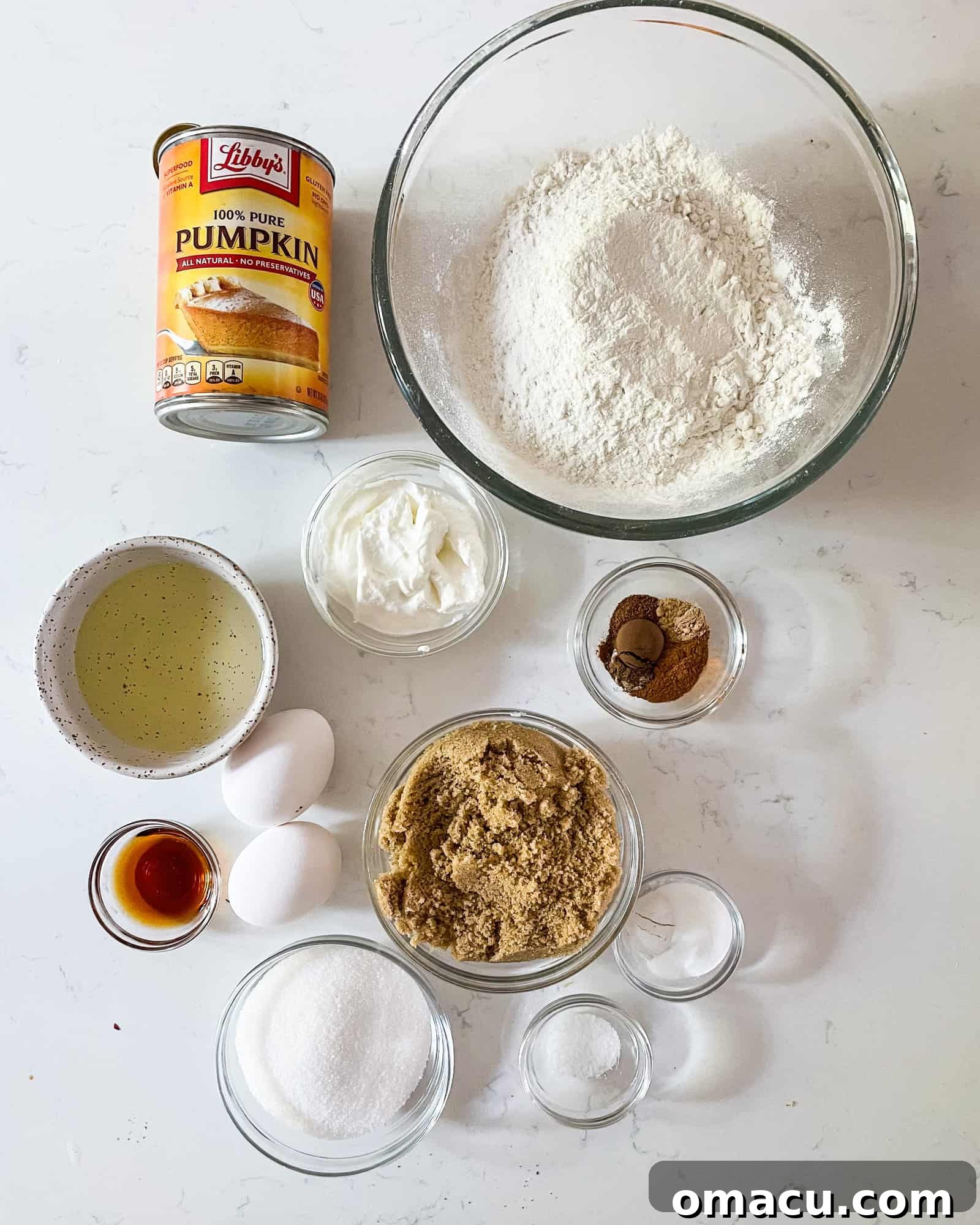 Various ingredients for pumpkin muffins, including flour, sugar, spices, and pumpkin puree, neatly arranged in separate bowls, ready for mixing.