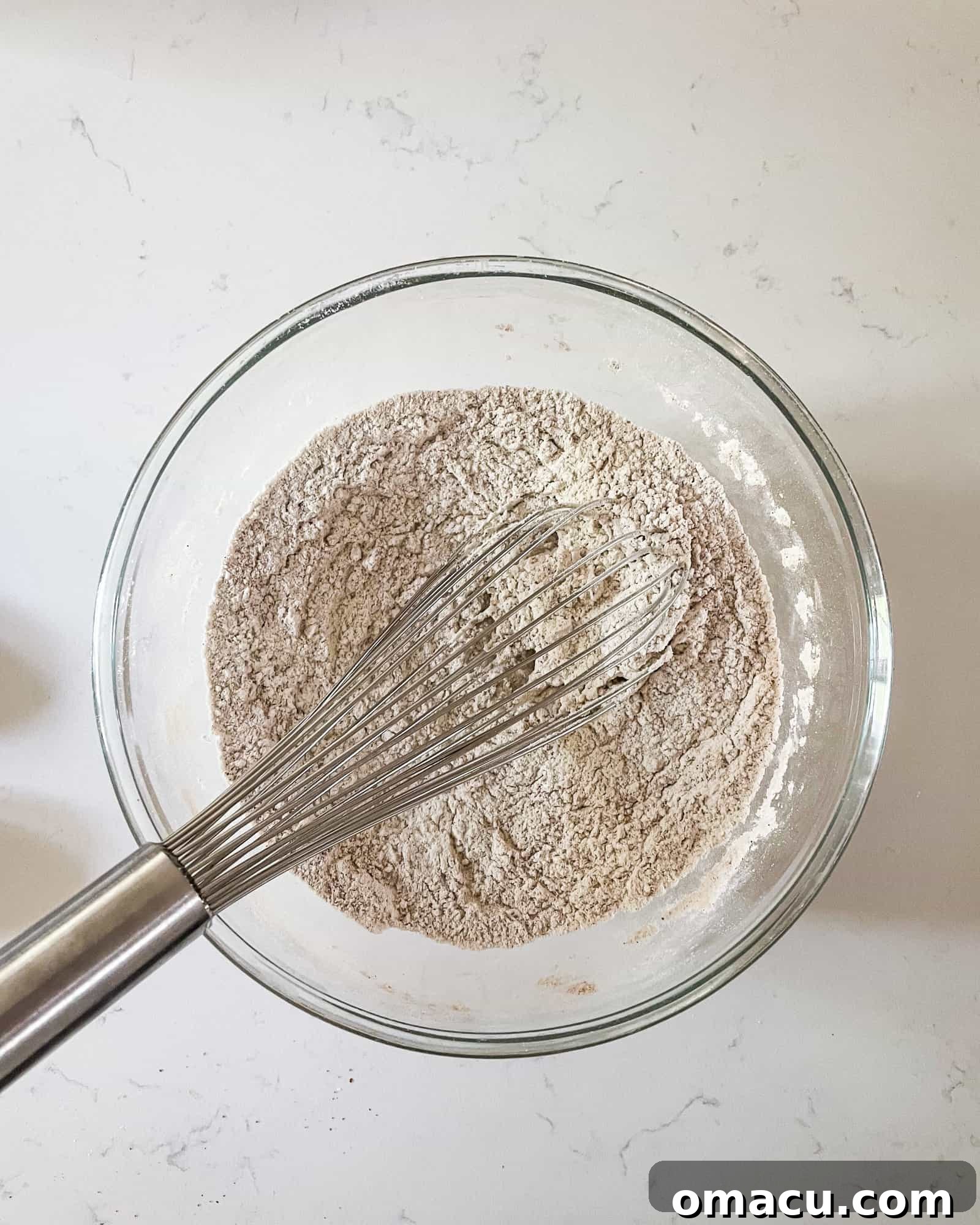 Dry ingredients for pumpkin muffins, including flour and various spices, expertly whisked together in a large mixing bowl, ready for the next step.