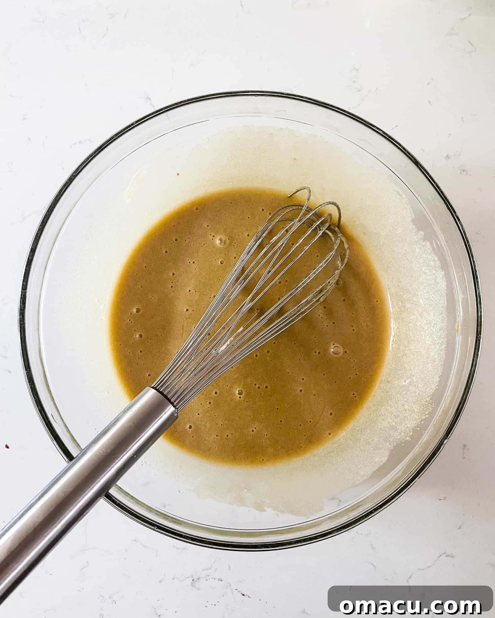 Wet ingredients for pumpkin muffins, including sugar, oil, and sour cream, blended smoothly in a bowl, showing the initial creamy texture.