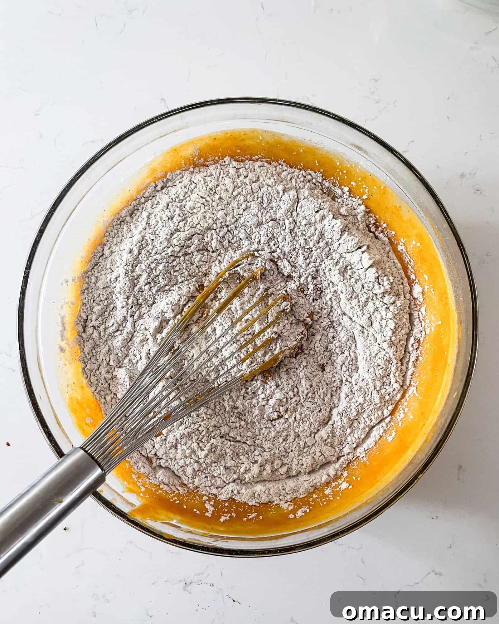 Dry and wet pumpkin muffin ingredients freshly mixed together in a large bowl, forming a smooth, ready-to-bake batter.