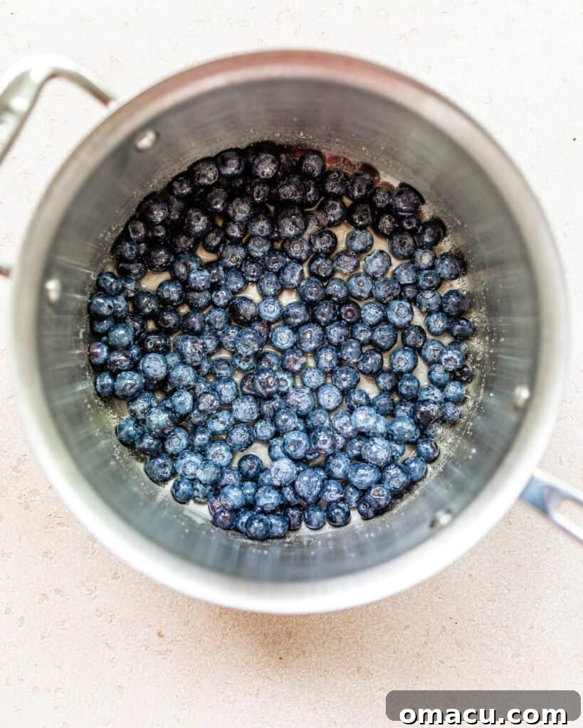 Fresh blueberries simmering in a saucepan with sugar and lemon juice, forming the rich compote.