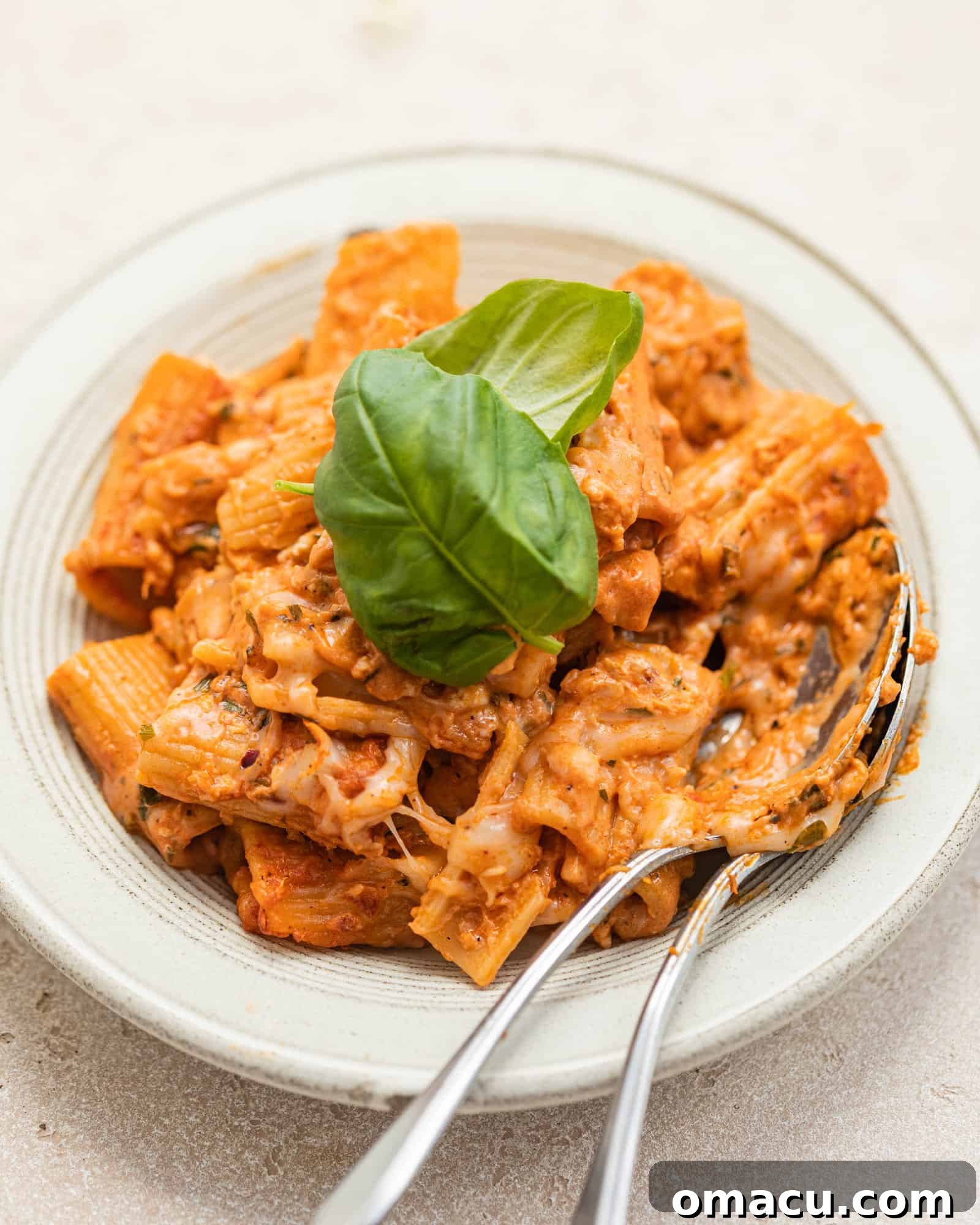 A plate of buffalo chicken pasta ready to eat, with two spoons for serving