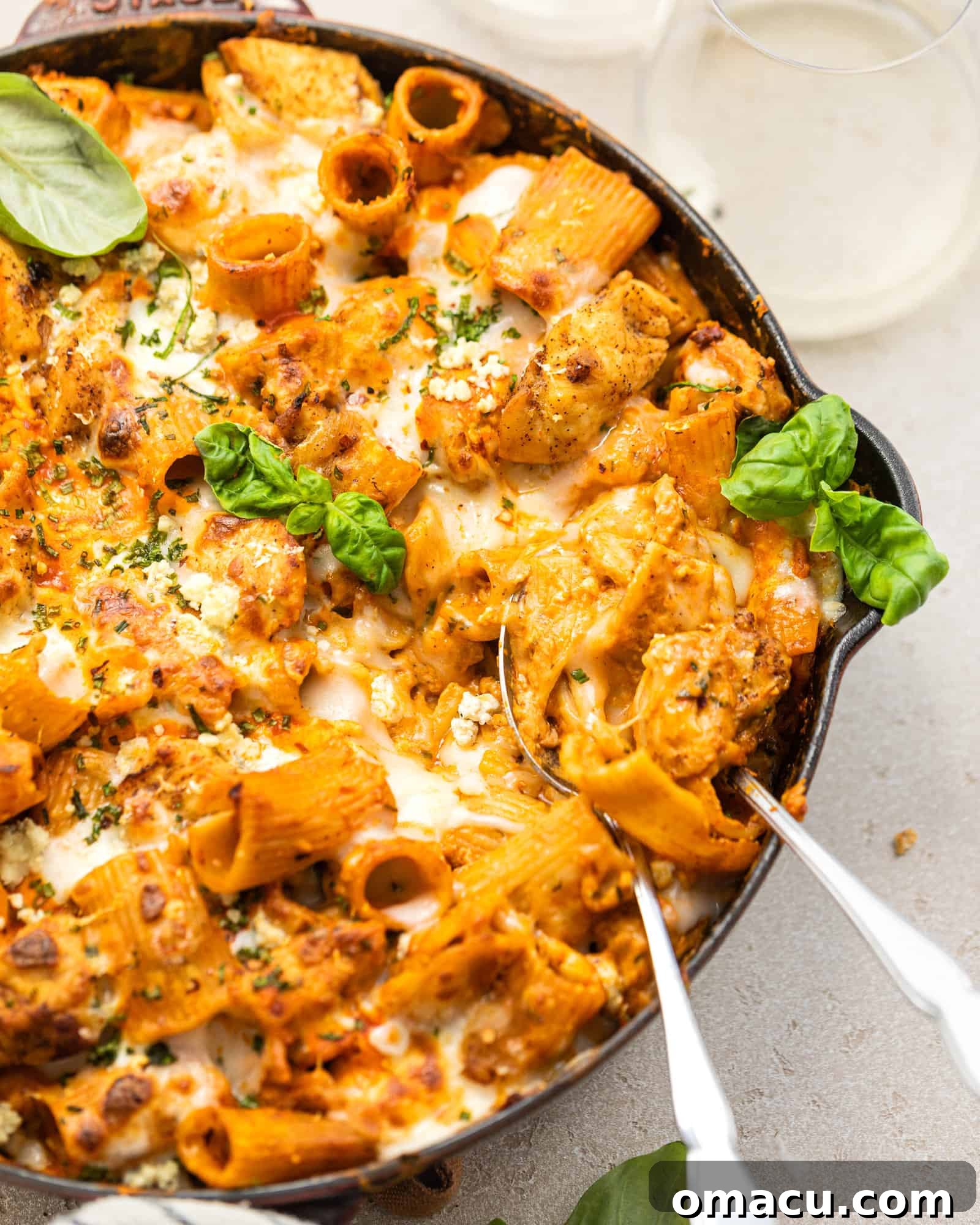 Large skillet of buffalo chicken pasta with two serving spoons, garnished with fresh herbs