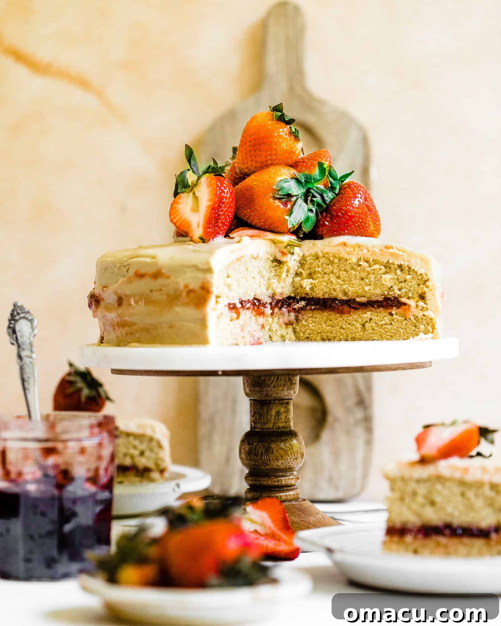 A beautifully decorated Strawberry Jam Cake on a cake stand, adorned with fresh strawberries, ready to be served.