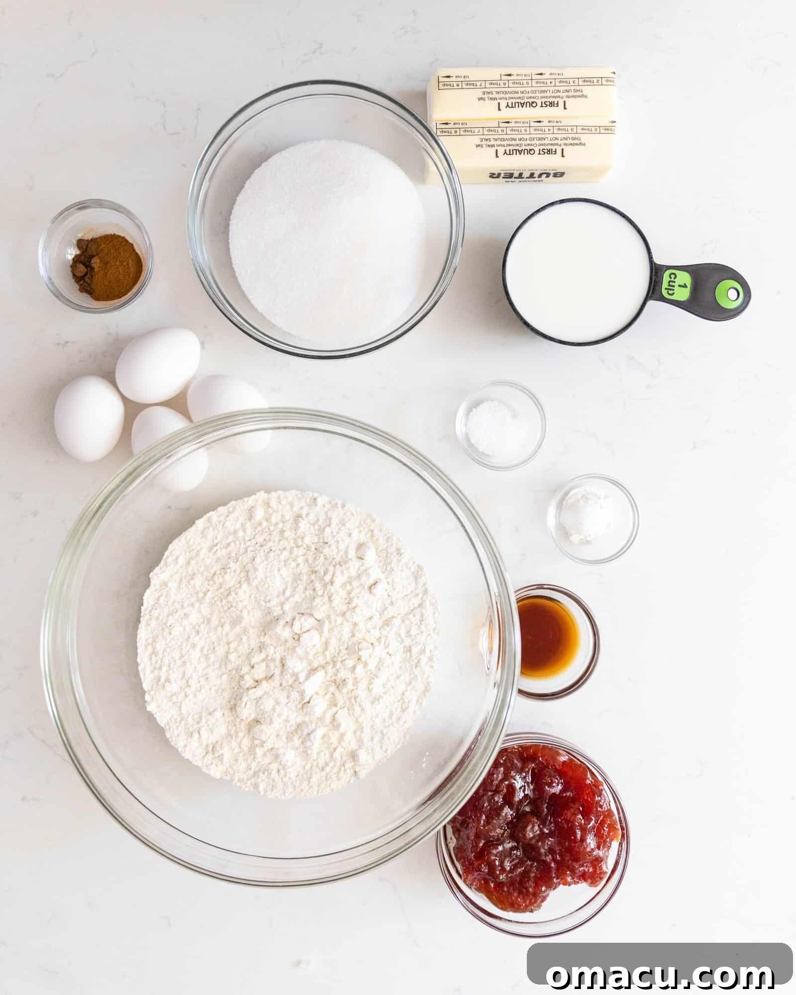 An assortment of fresh ingredients laid out, including flour, sugar, butter, eggs, and spices, ready to be transformed into a homemade Jam Cake.