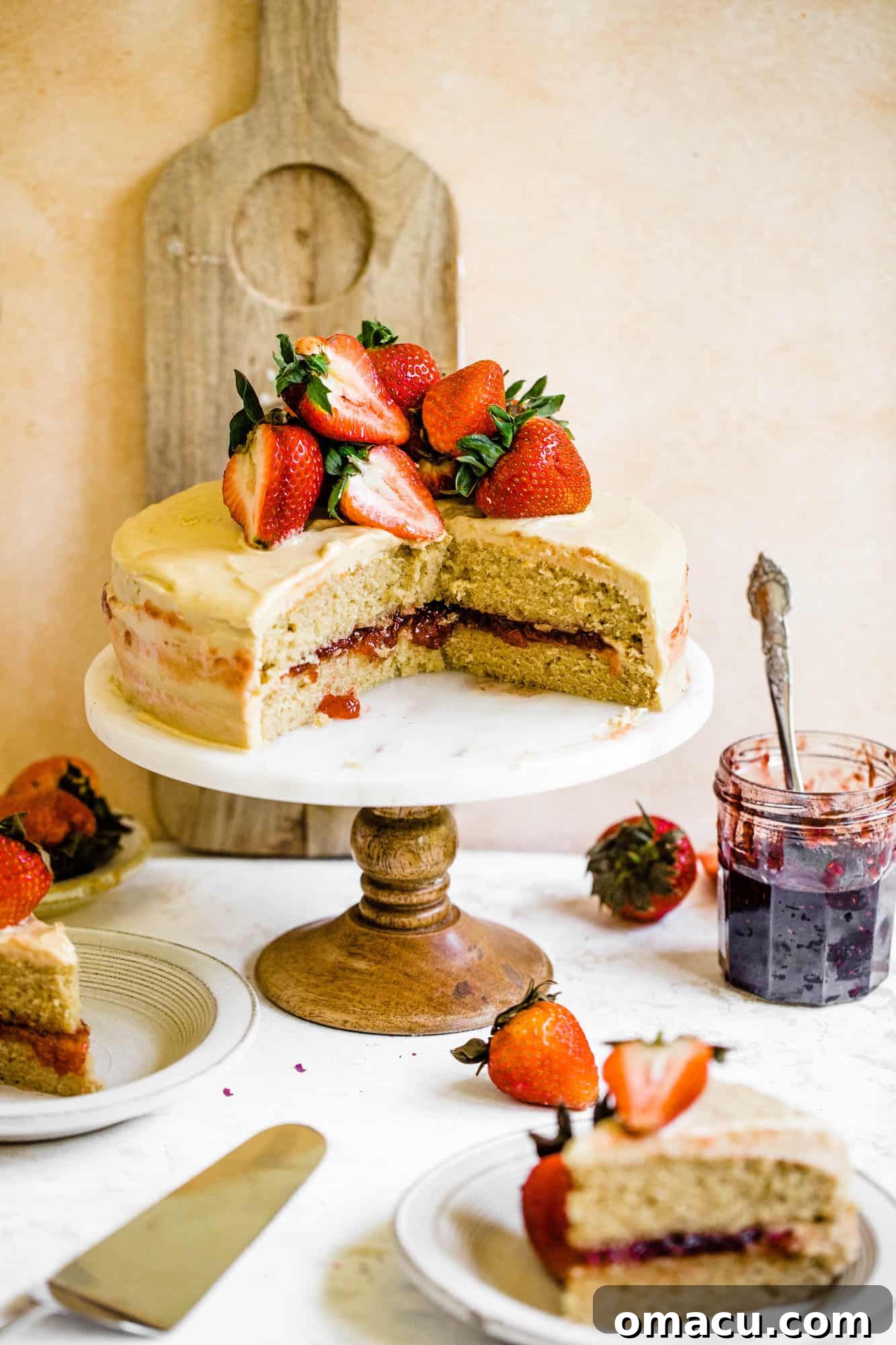 A stunning Strawberry Jam Cake displayed on a cake stand, with individual slices plated nearby, showcasing its beautiful layers and vibrant filling.