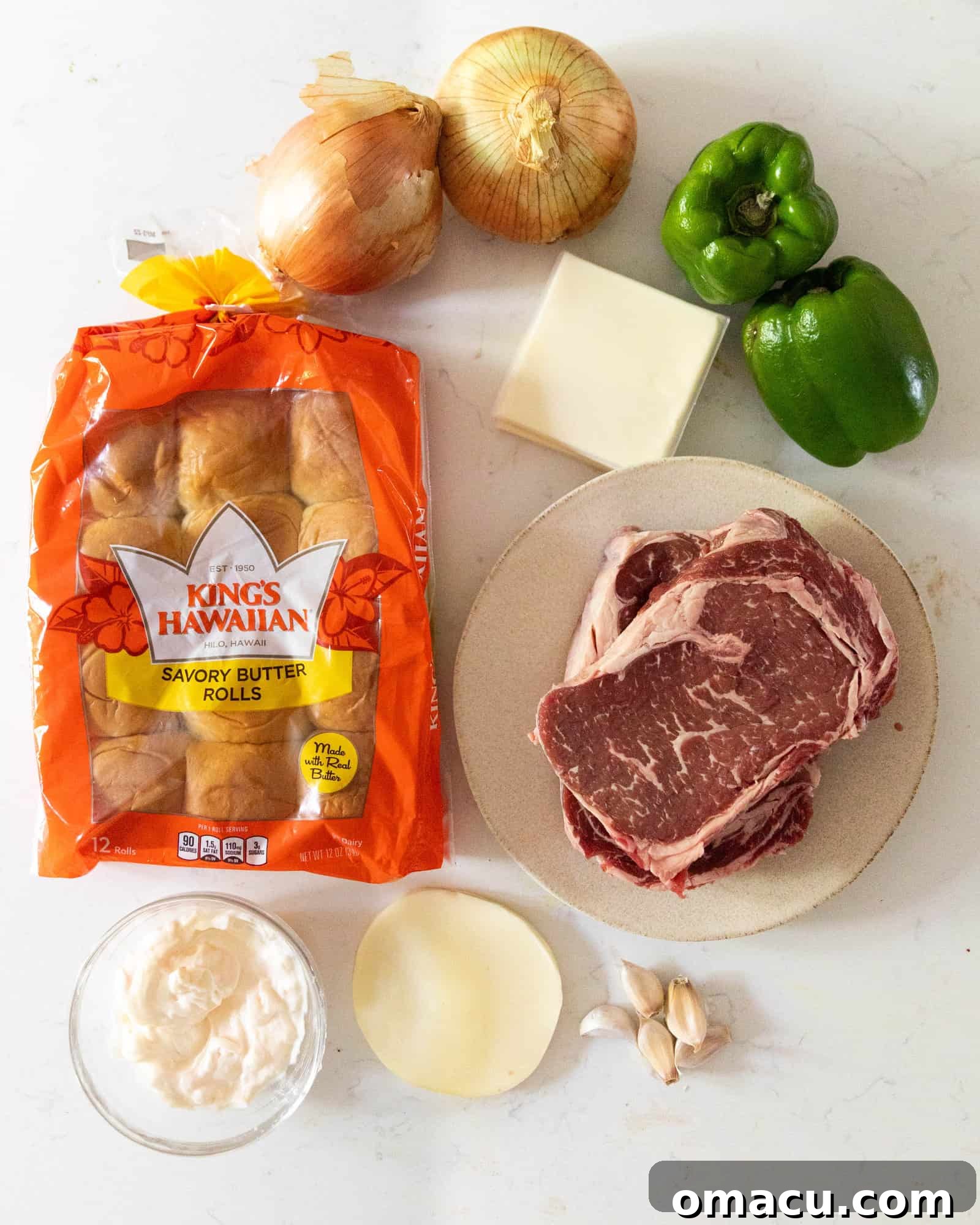 Various fresh ingredients laid out on a white surface, ready to make Philly Cheesesteak Sliders