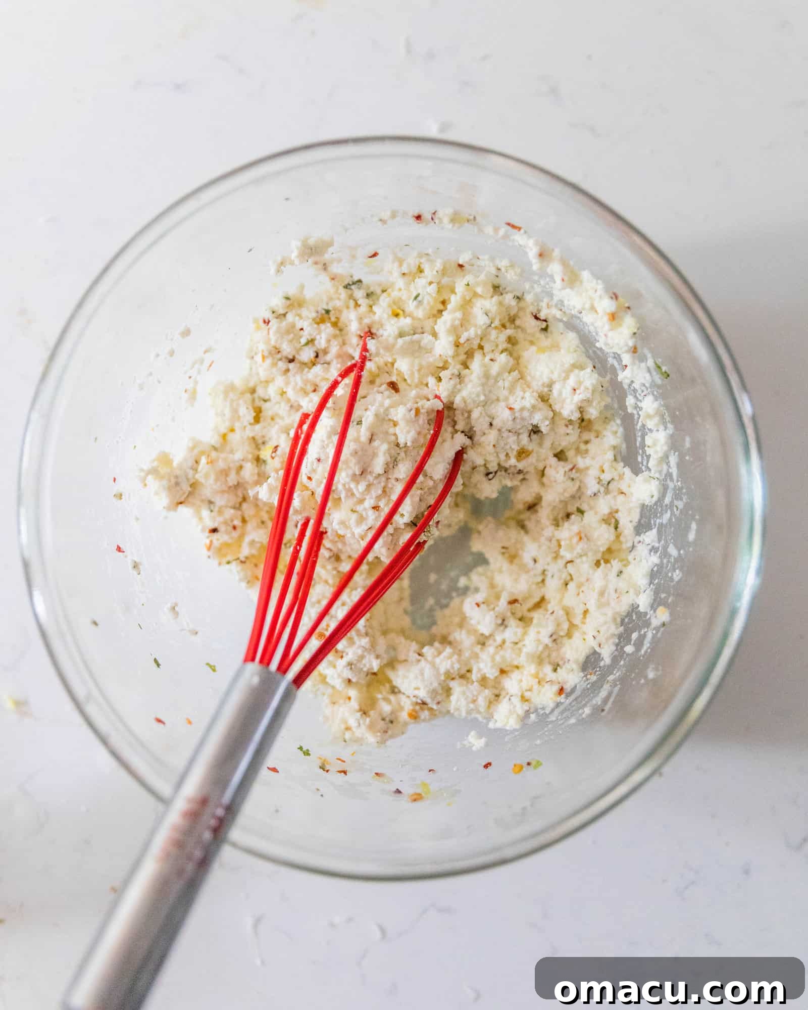 A bowl of creamy ricotta sauce being whisked, showcasing its smooth and inviting texture.