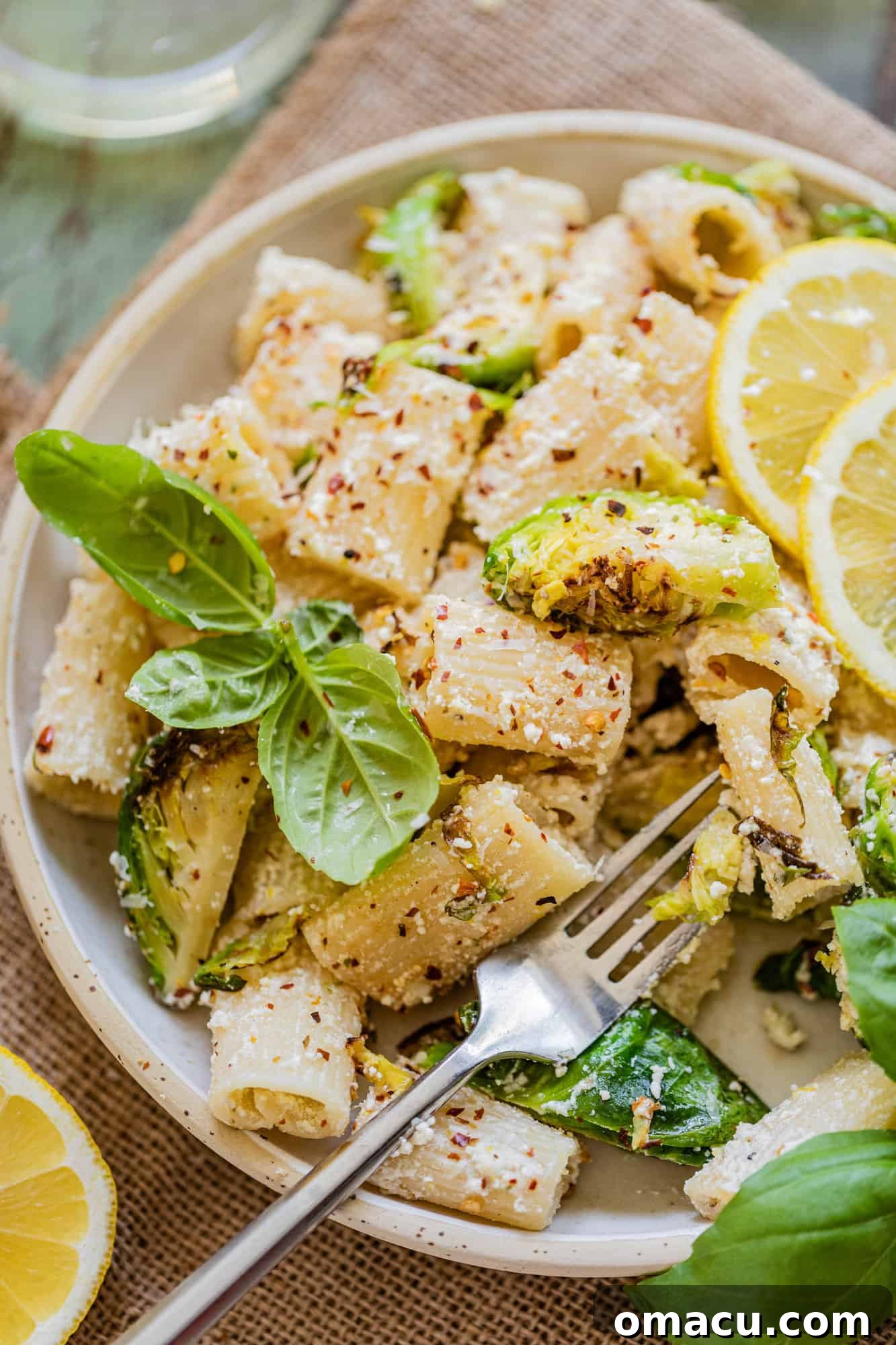 A single serving of pasta on a white plate, adorned with lemon wedges and fresh basil, highlighting its inviting appearance.