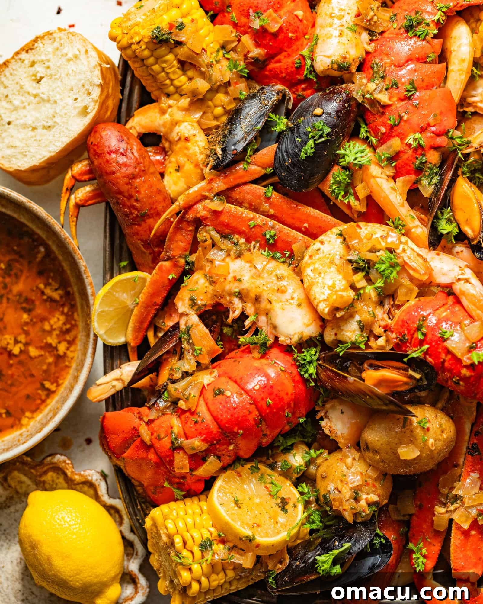 A vibrant cajun seafood boil served on a large tray, generously covered in a rich garlic butter sauce, surrounded by sliced lemons and fresh bread.