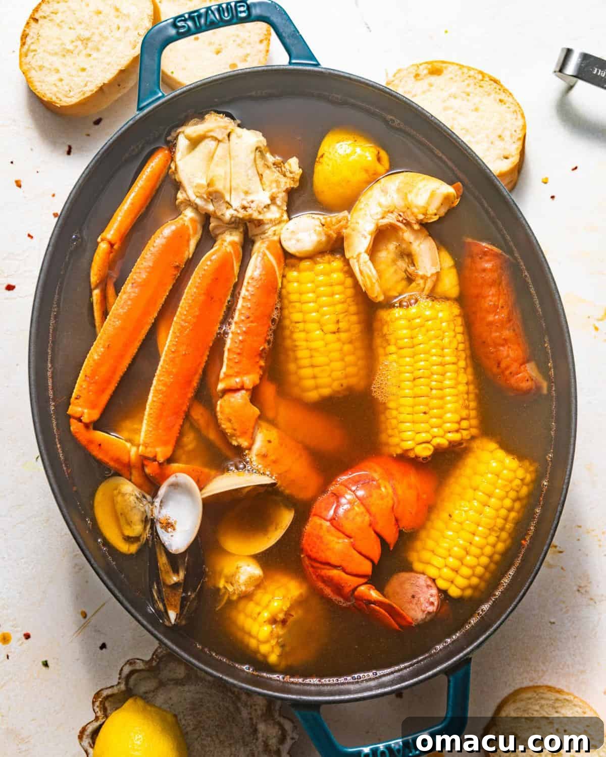 Overhead shot of various seafood, including crab legs, lobster tails, mussels, clams, and shrimp, freshly added to a large pot of boiling seasoned broth to complete the seafood boil.