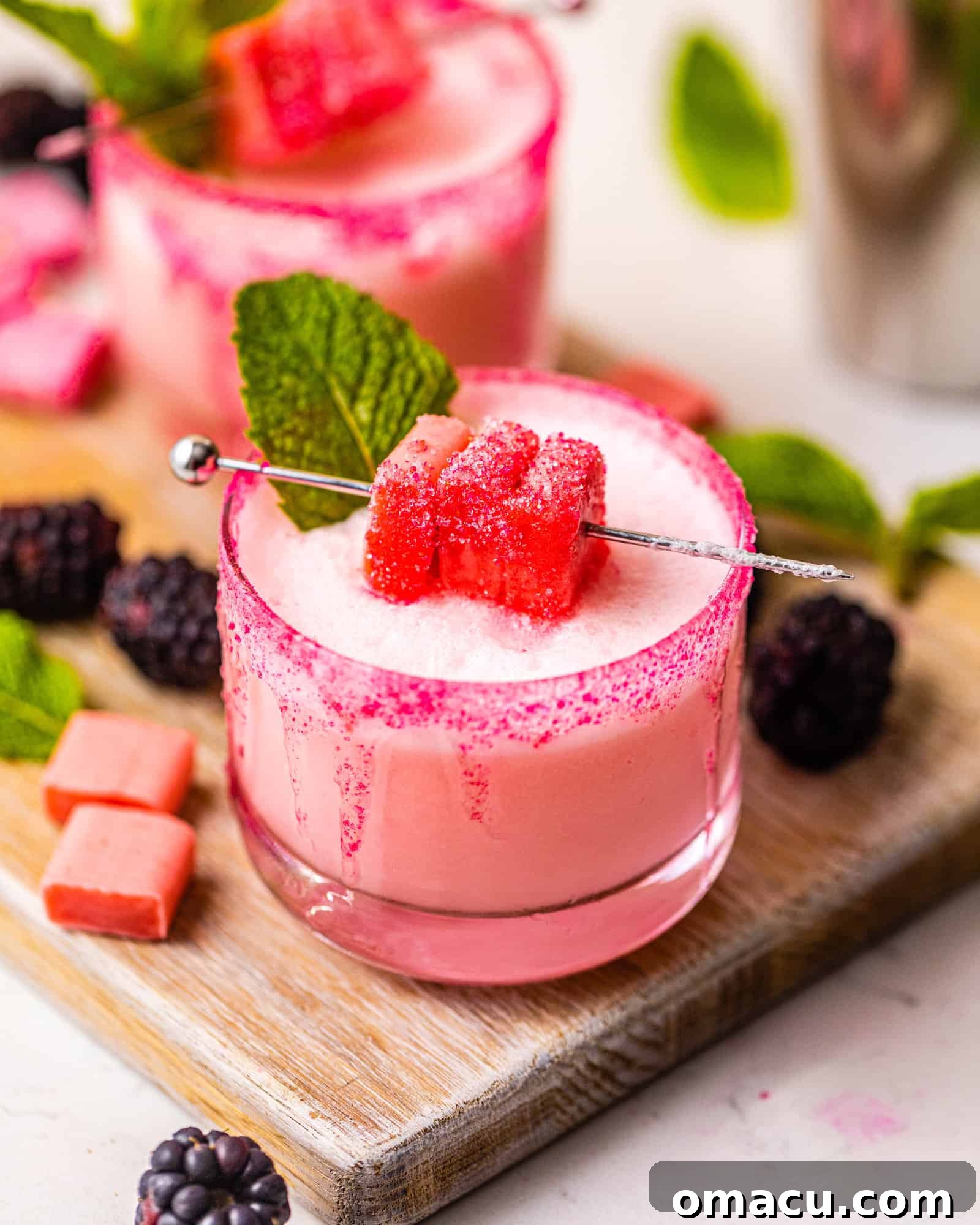A vibrant pink Starburst shot in a pink sugar-rimmed glass, garnished with Starburst candy, resting elegantly on a rustic wood tray.
