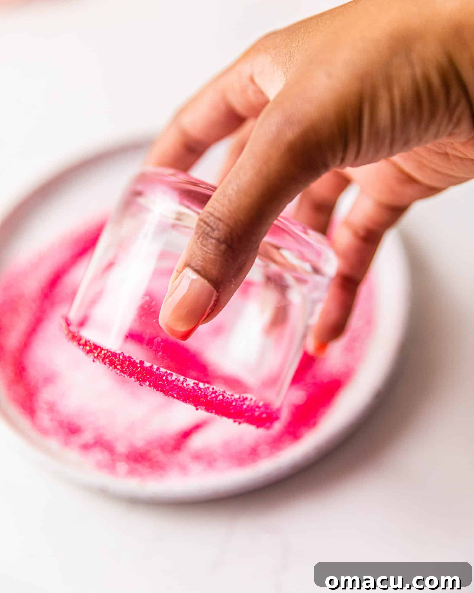 A hand carefully holding a cocktail glass with a perfectly crafted pink sugar rim.