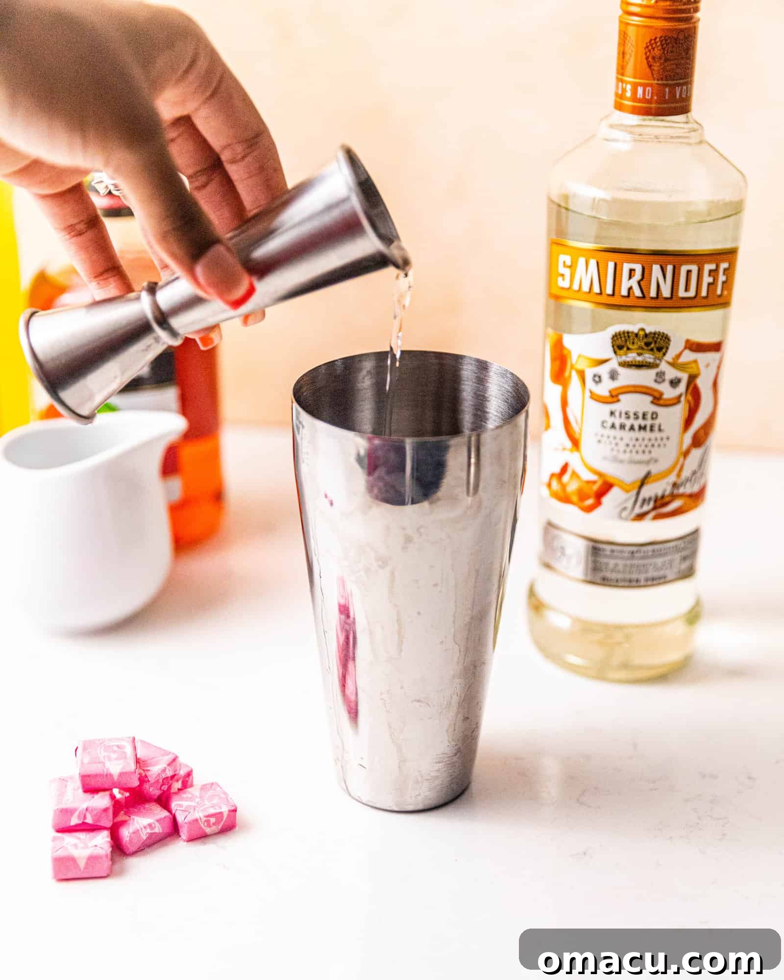 Pouring Kissed Caramel Vodka into a cocktail shaker as part of the Starburst shot preparation.