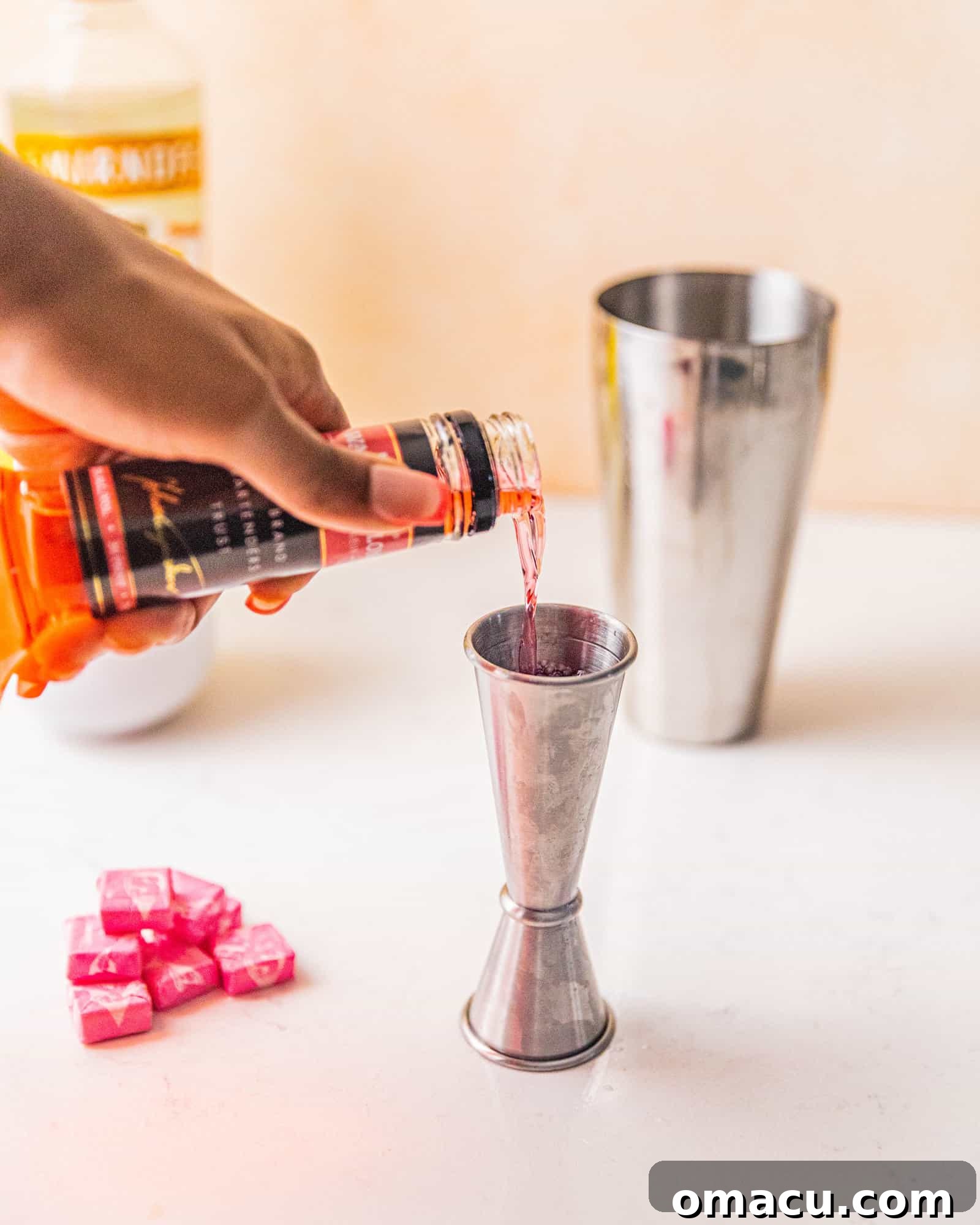 Pouring vibrant Watermelon Pucker Schnapps into a jigger for precise measurement.