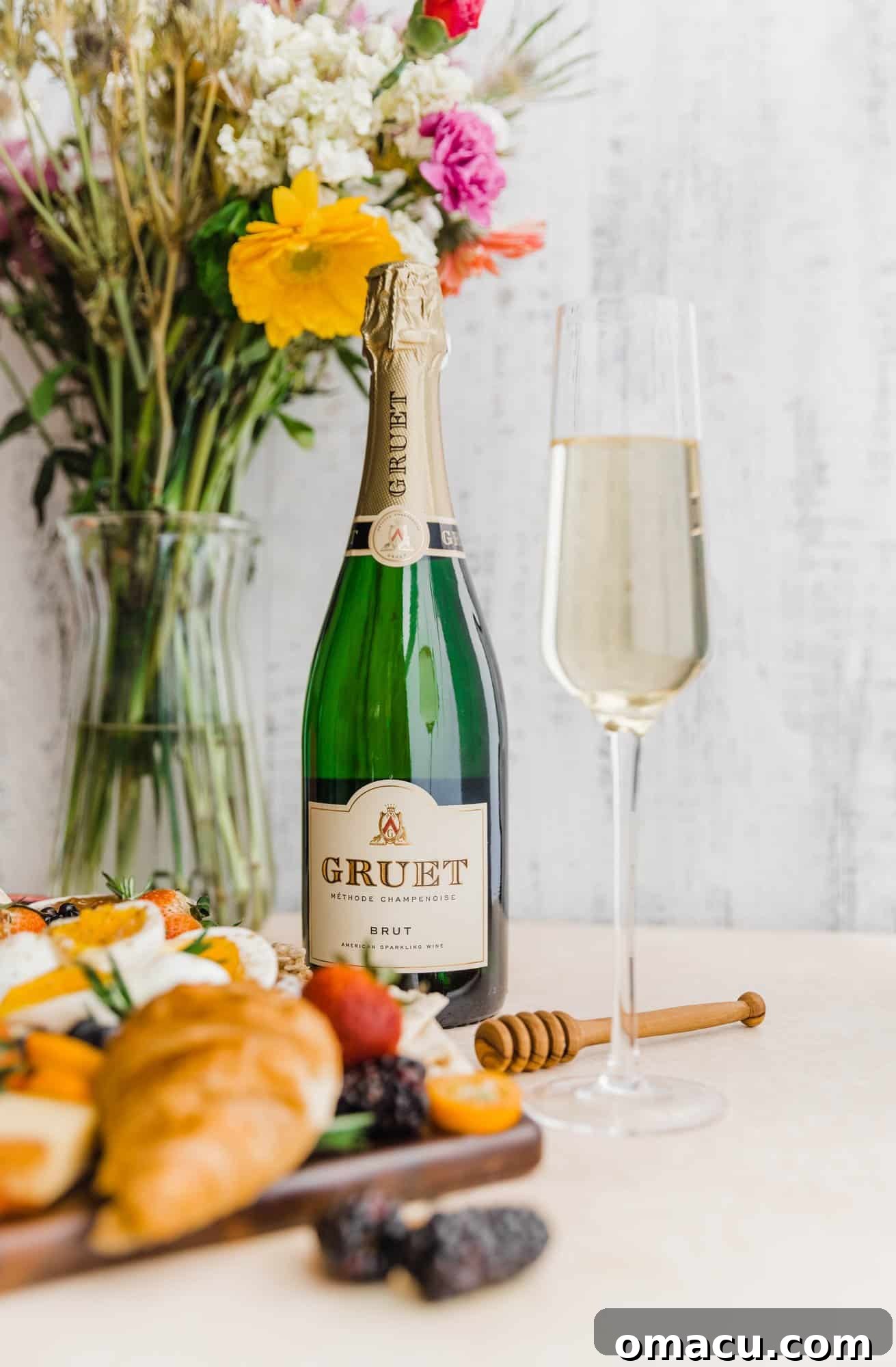 A bottle of sparkling champagne casually placed under a vibrant bouquet of flowers, with a single champagne flute ready for pouring.