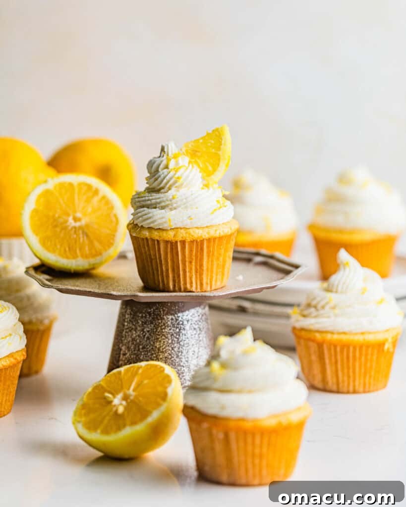 Three beautifully decorated lemon drizzle cupcakes on a small white cake stand, garnished with fresh lemon slices, highlighting their vibrant appeal and deliciousness.