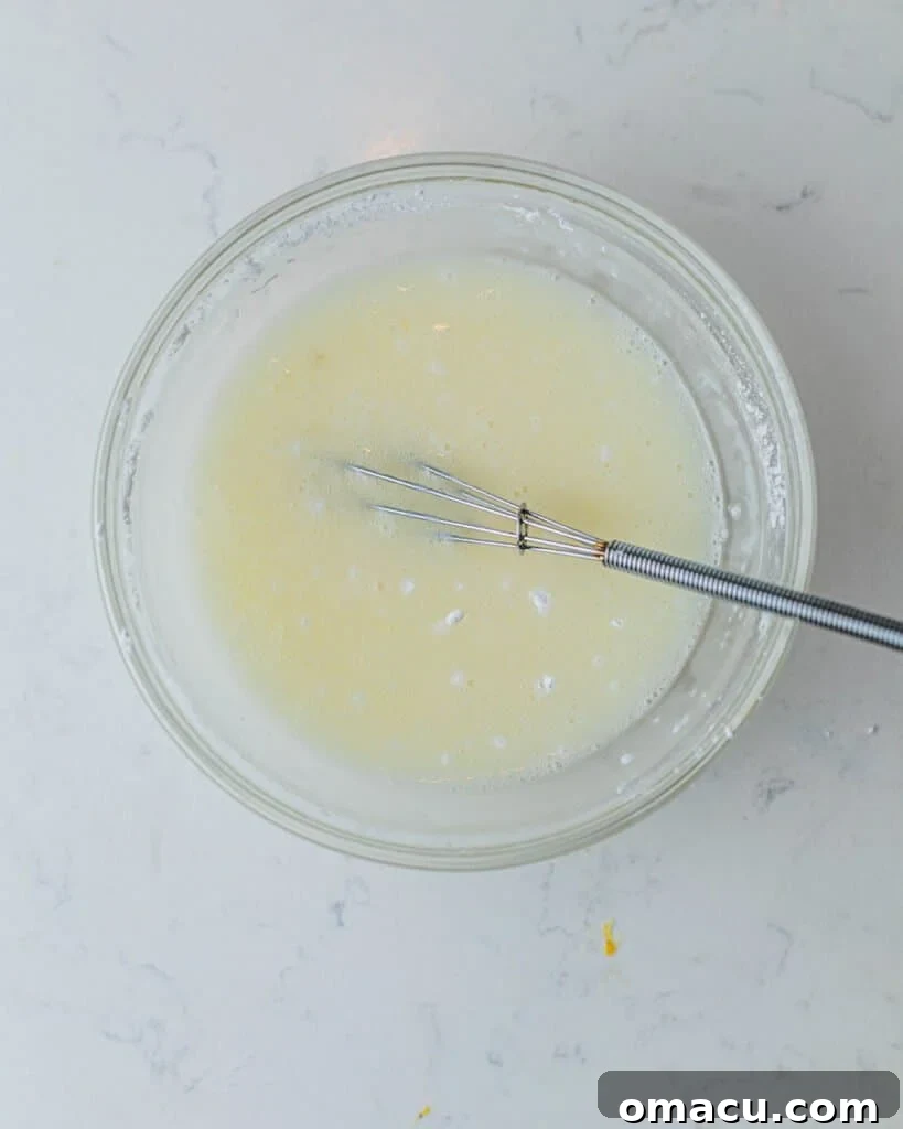 A small bowl containing the cloudy, translucent lemon drizzle, perfectly mixed and ready to be applied to the cupcakes.