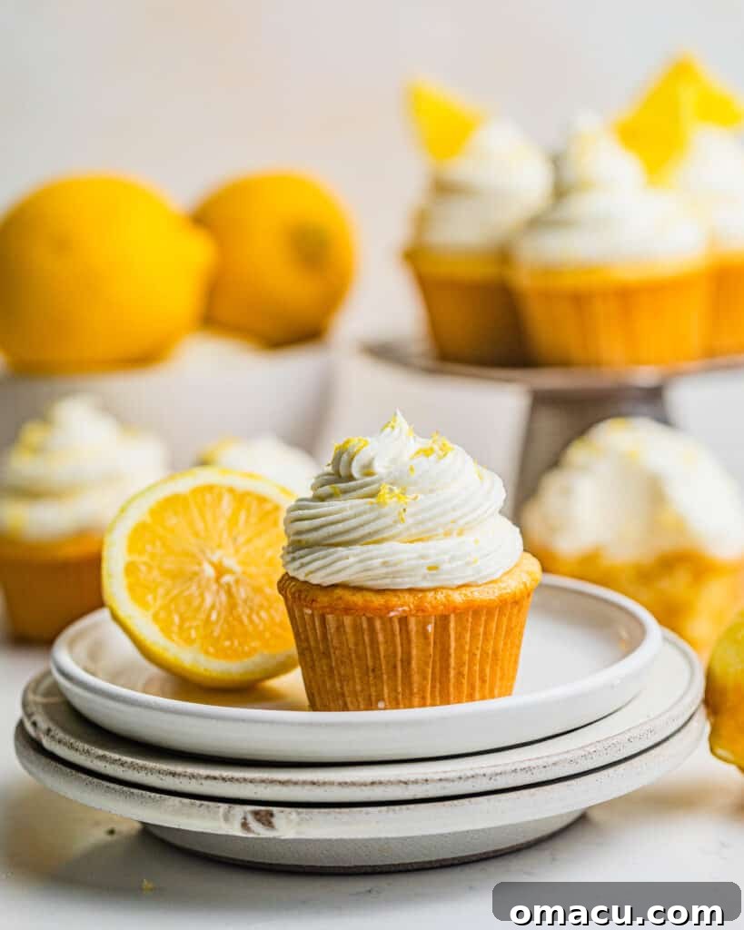 A single lemon drizzle cupcake on a plate, with more cupcakes blurred in the background, inviting you to indulge in this zesty dessert.