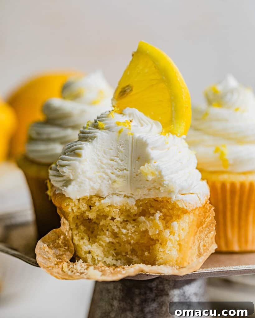 A close-up shot of three lemon drizzle cupcakes on a small cake stand, one with a bite taken out, revealing the moist interior and fluffy texture, emphasizing their irresistible nature.