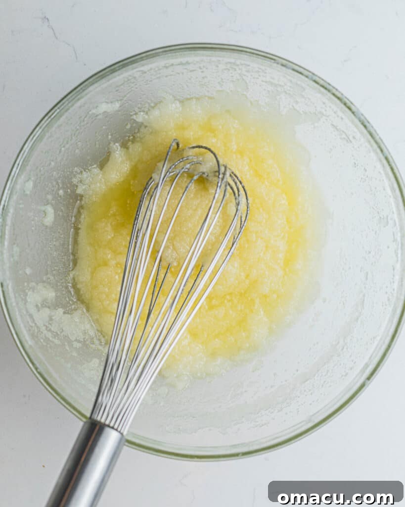 Step-by-step image: Butter, oil, and sugar being creamed together in a mixing bowl with a whisk, showing the initial stage of preparing the cupcake batter.