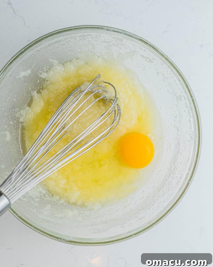 Step-by-step image: Cupcake batter in a bowl with a cracked egg, illustrating the process of adding eggs one by one to the wet ingredients.