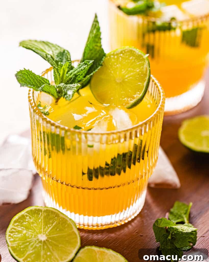 Close-up photo of a Mango Mojito garnished with mint leaves and fresh limes, showing condensation on the glass.