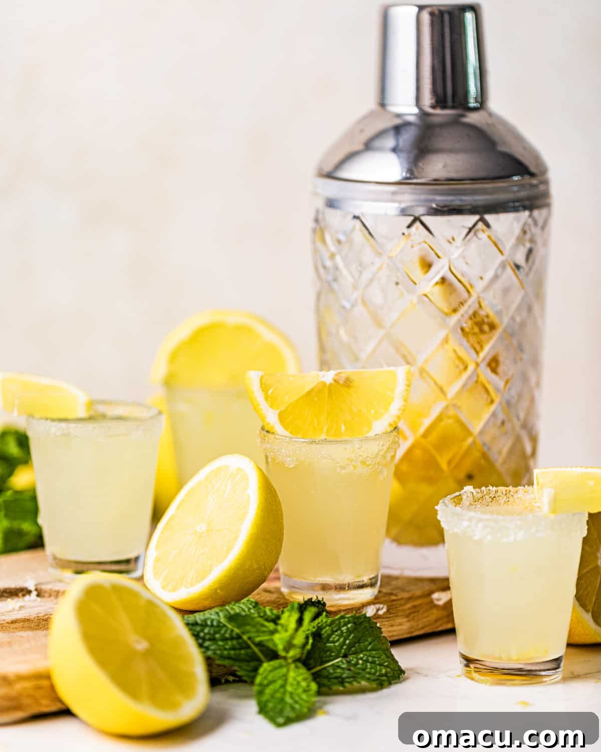 A single lemon drop shot artfully arranged on a rustic wooden serving board with scattered lemon slices.