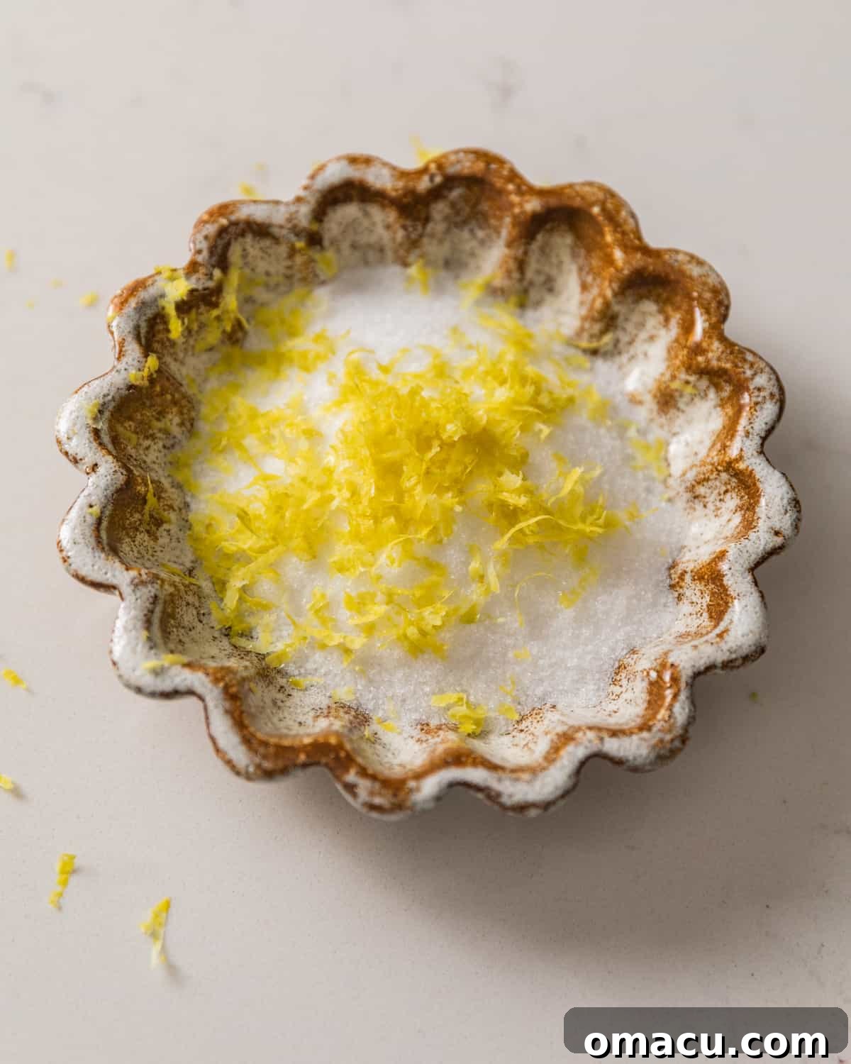 Finely grated lemon zest mixed with white sugar in a small ceramic bowl.