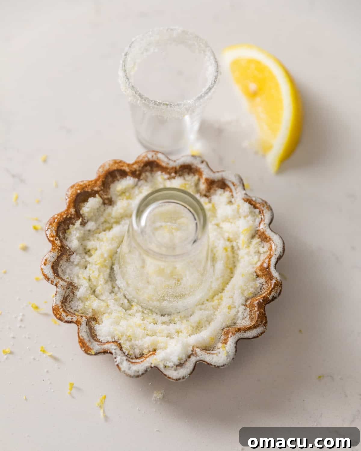 A shot glass being carefully dipped into a bowl of lemon sugar to create a decorative and flavorful sugar rim.