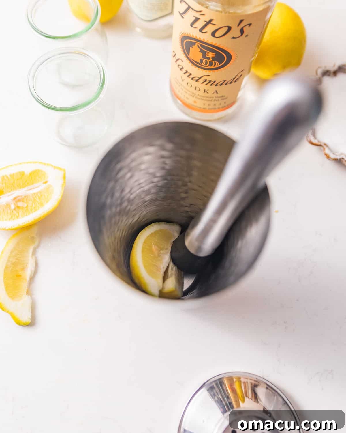 Fresh lemon wedges being actively muddled at the bottom of a stainless steel cocktail shaker.