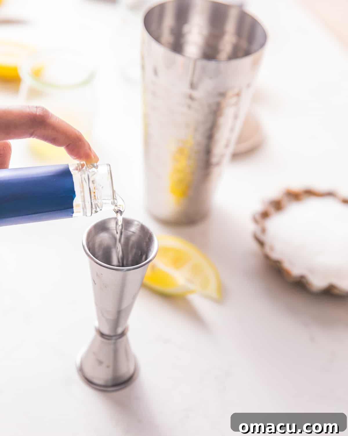 A hand pouring golden simple syrup from a measuring jigger into a cocktail shaker.