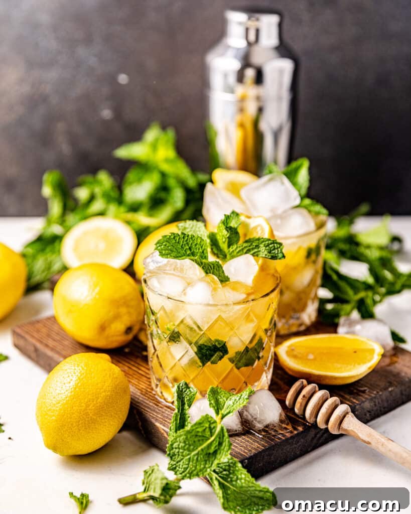 A vibrant Bourbon Smash cocktail served on a rustic brown tray, accompanied by fresh mint leaves, bright sliced lemons, and sparkling ice cubes, ready to be enjoyed.