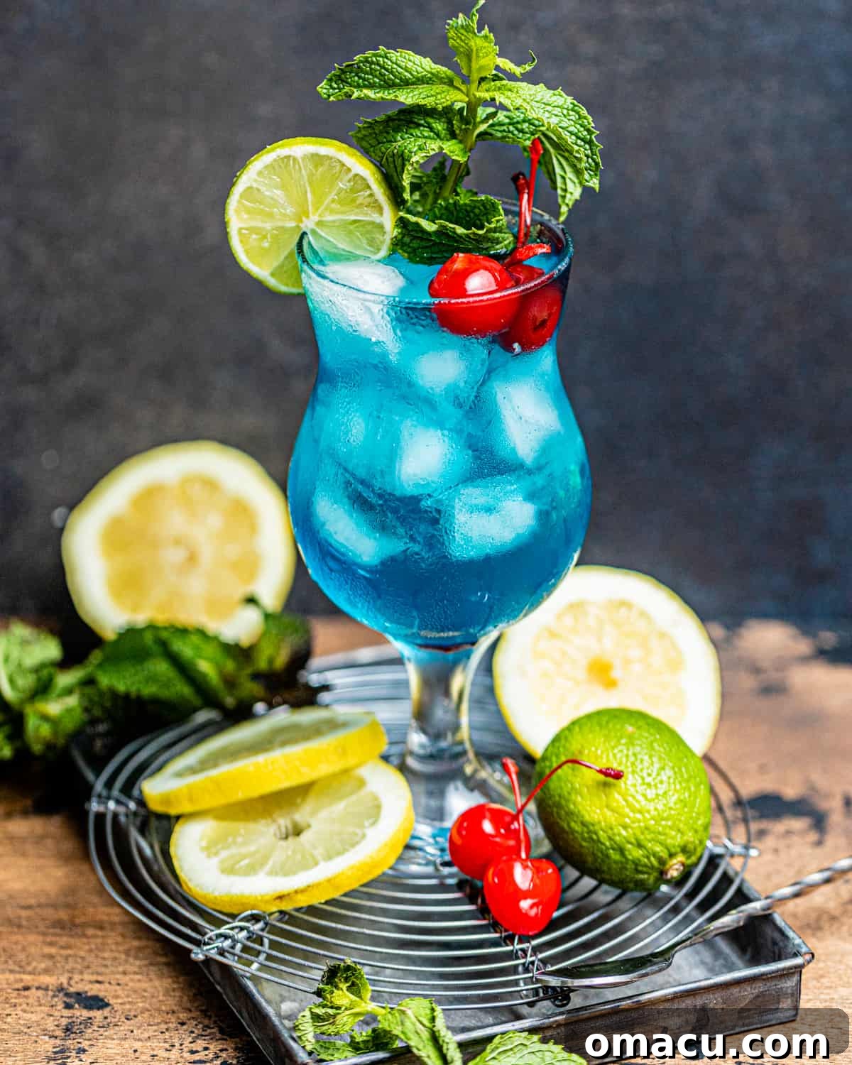 An AMF Drink on a brown surface garnished with fresh mint, maraschino cherries, and a lime wedge.