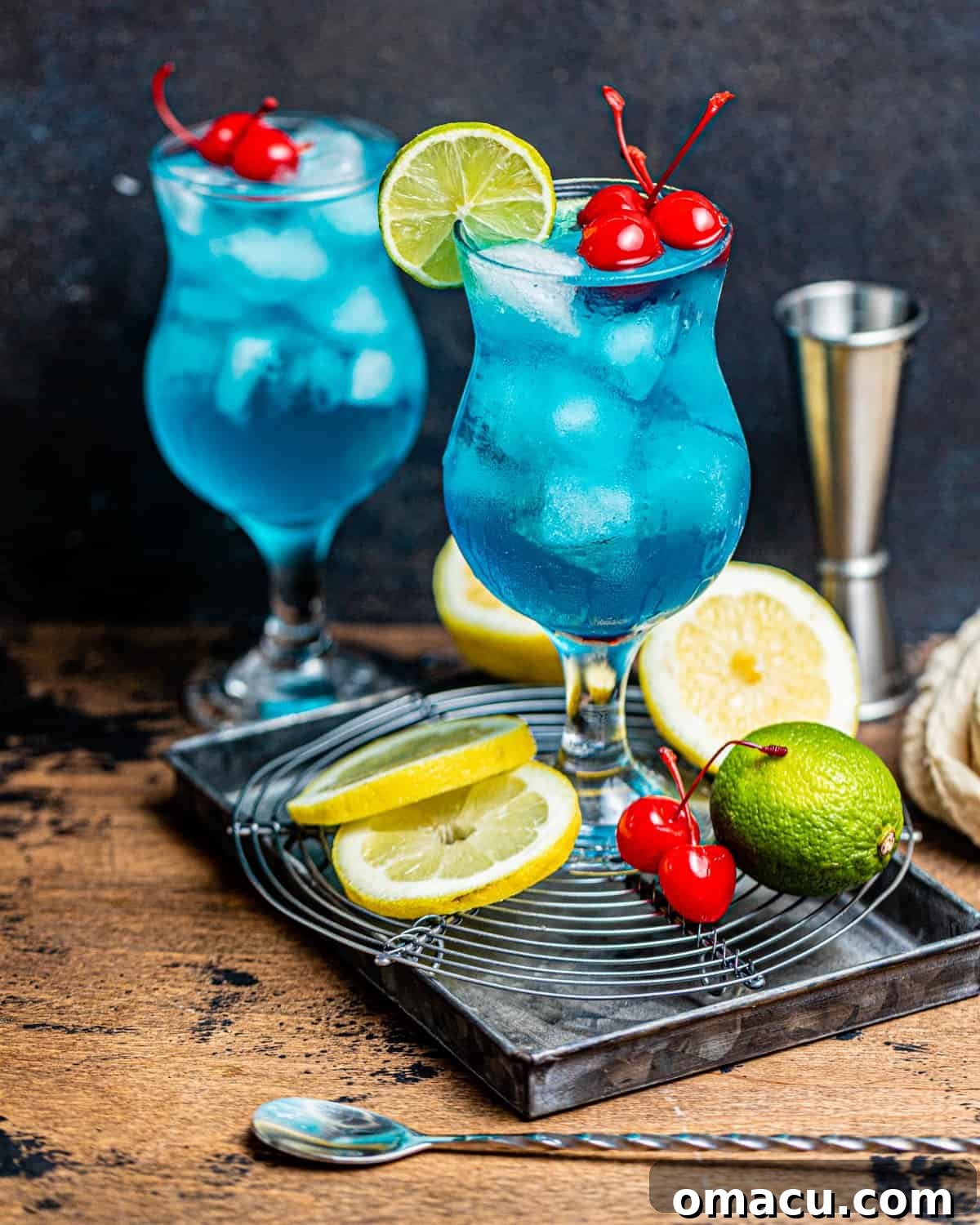 Two AMF drinks on a brown surface with sliced lemons and cherries.