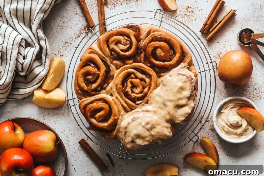 Close-up of golden brown Apple Cider Cinnamon Rolls in a baking dish, glistening with frosting.