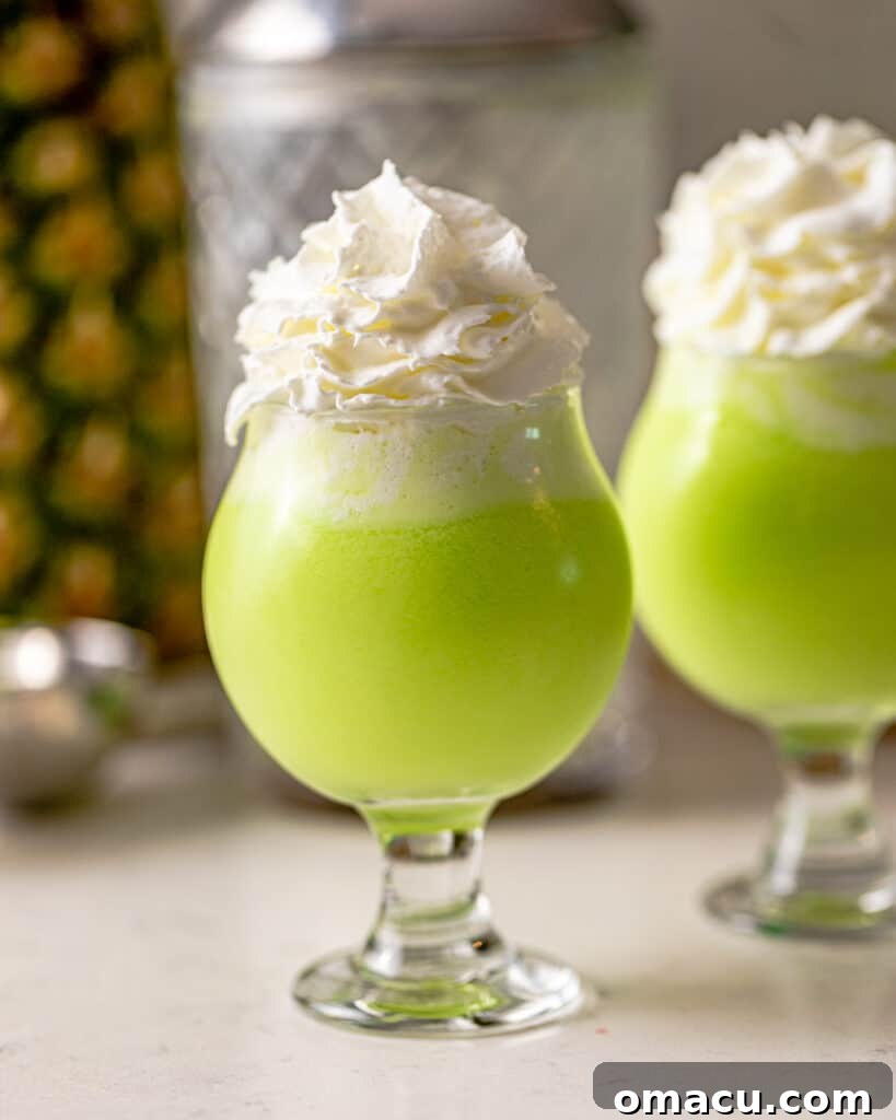 An artistic close-up photo of a single Scooby Snack Shot in a small glass, perfectly layered with whipped cream and a cherry, highlighting its creamy green color.