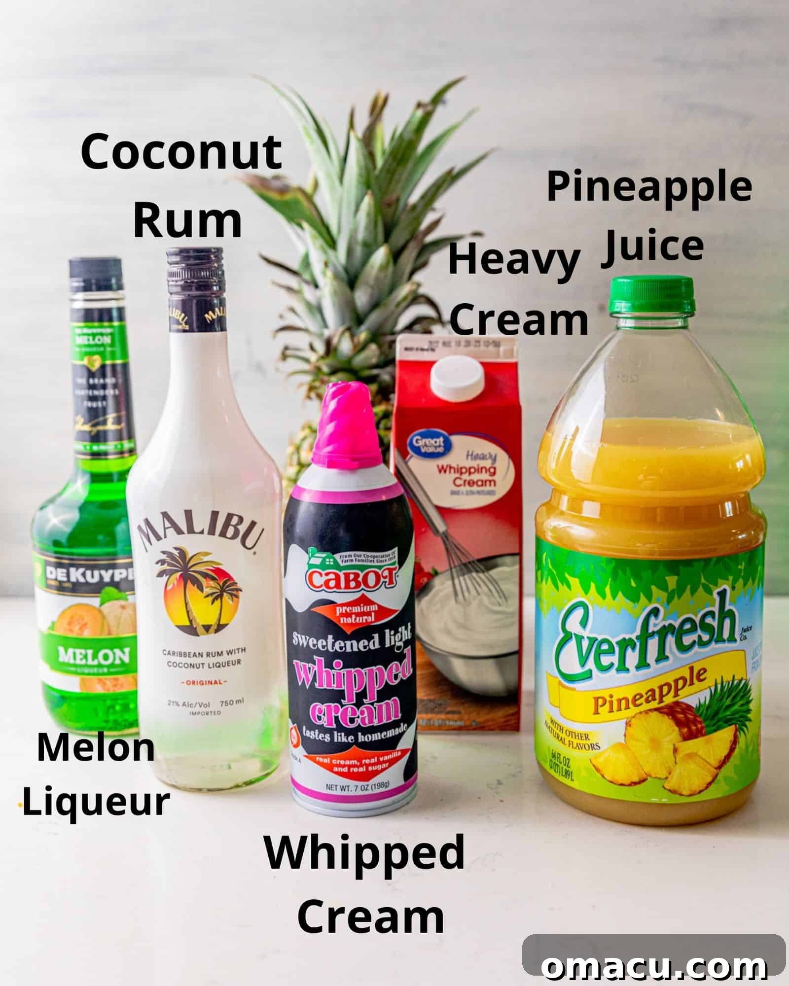 All the essential ingredients for making a Scooby Snack Shot laid out: a bottle of coconut rum, melon liqueur, heavy cream, pineapple juice, and a can of whipped cream.