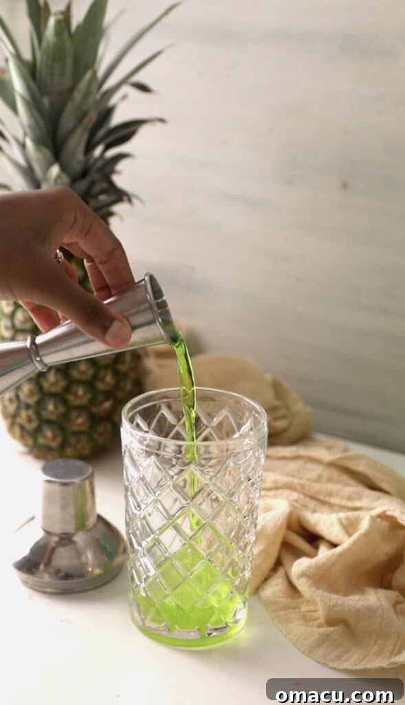 Adding a vibrant green stream of melon liqueur to the cocktail shaker, mixing with the rum.